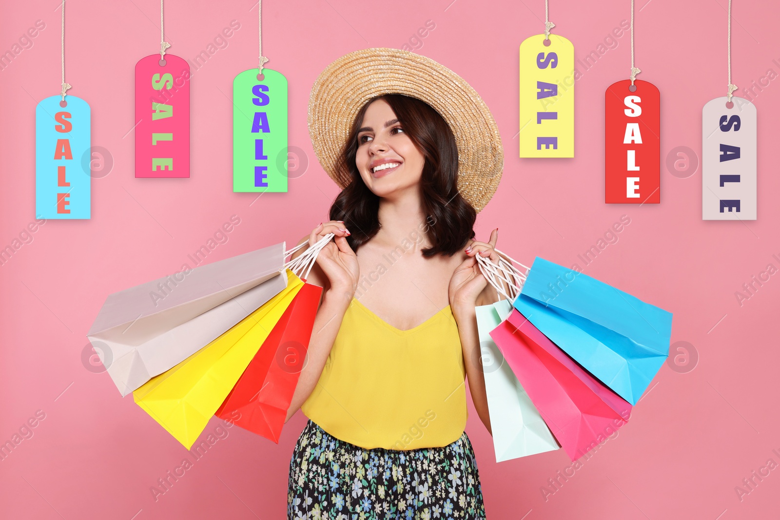 Image of Beautiful young woman with paper shopping bags and Sale labels on pink background