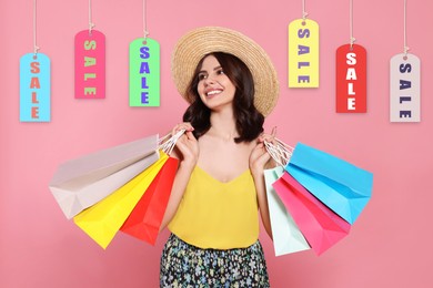 Beautiful young woman with paper shopping bags and Sale labels on pink background