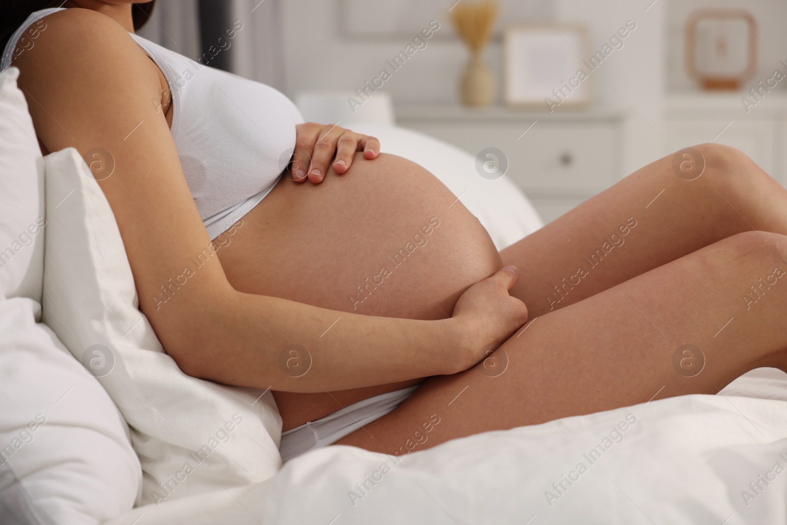 Photo of Pregnant woman in stylish comfortable underwear on bed at home, closeup