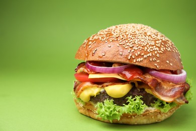 Photo of Delicious burger with bacon, patty and vegetables on green background, closeup. Space for text