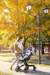 Photo of Happy mother with her baby daughter in stroller outdoors on autumn day