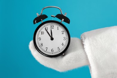 Santa Claus holding alarm clock on blue background, closeup. Christmas countdown