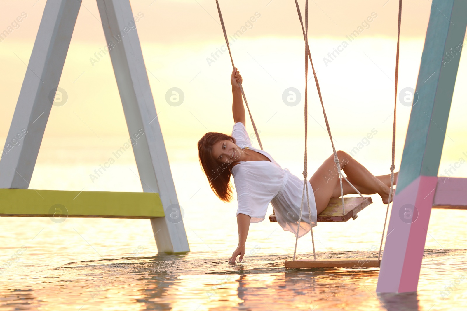 Photo of Young woman enjoying sunrise on swing over water