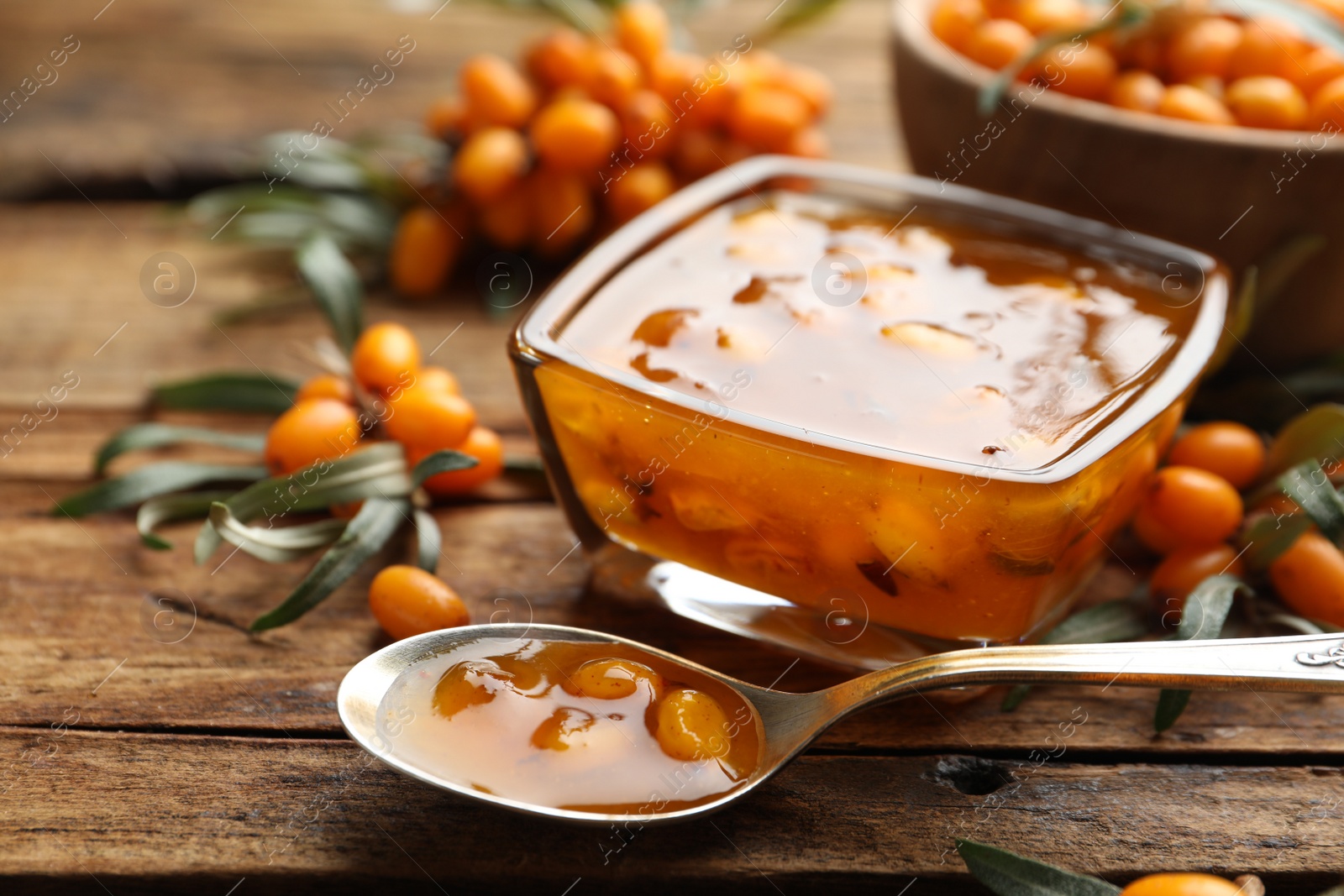 Photo of Delicious sea buckthorn jam and fresh berries on wooden table, closeup