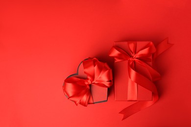 Beautiful gift boxes with bows on red background, flat lay. Space for text