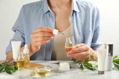 Photo of Woman dripping THC tincture or CBD oil into bottle at white marble table, closeup