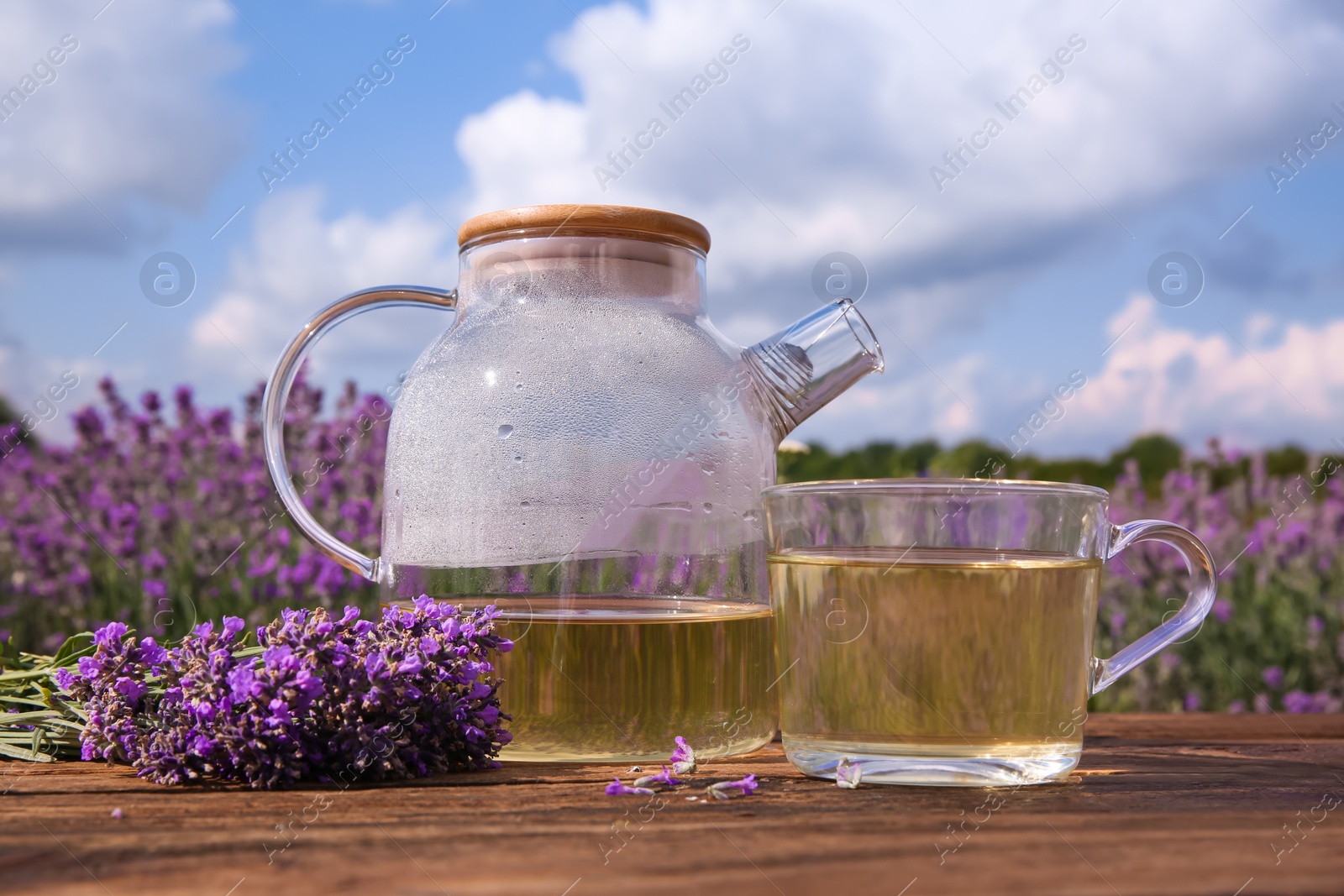 Photo of Tasty herbal tea and fresh lavender flowers on wooden table in field, closeup