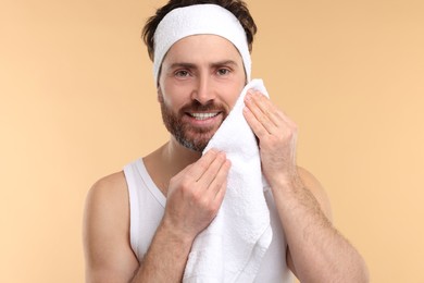 Photo of Washing face. Man with headband and towel on beige background