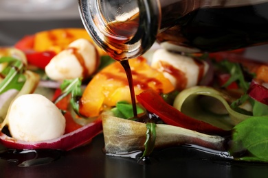 Photo of Pouring balsamic vinegar onto vegetable salad, closeup