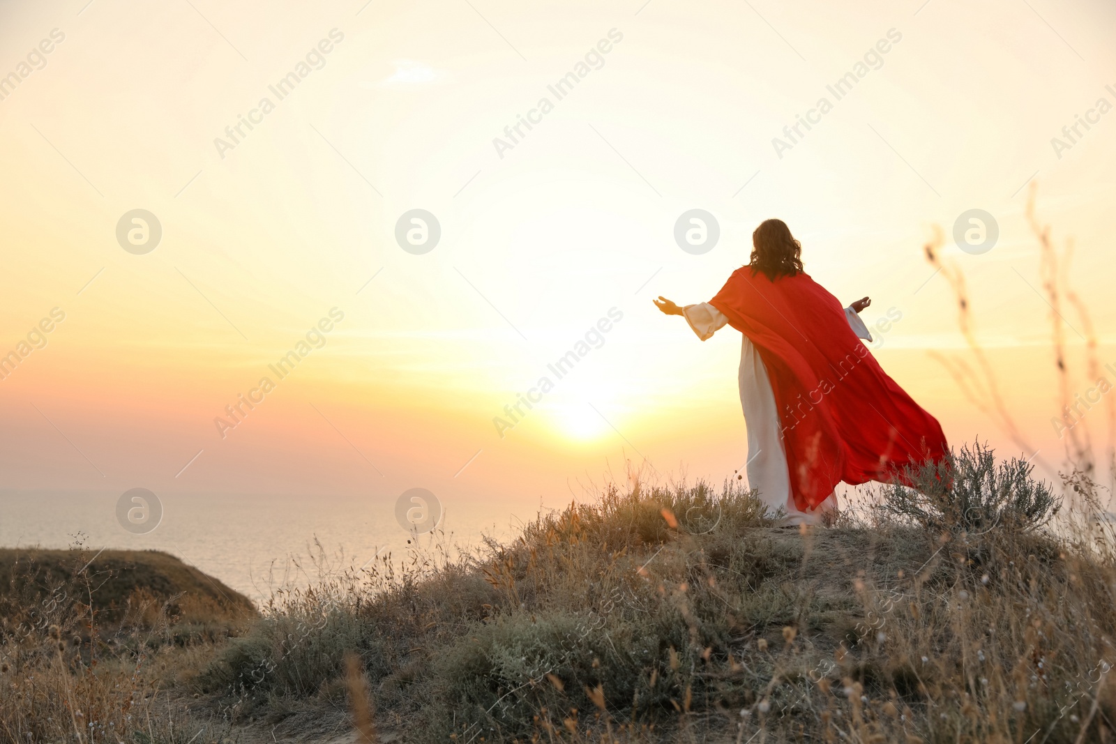 Photo of Jesus Christ raising hands on hills at sunset, back view. Space for text