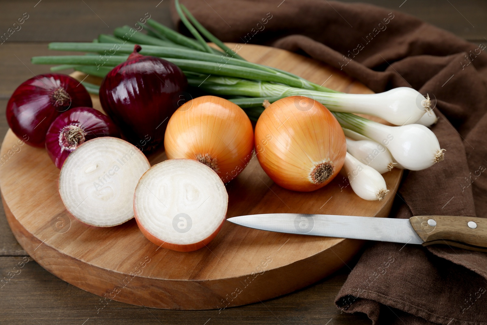 Photo of Board with different kinds of onions on wooden table, closeup