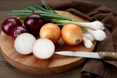 Photo of Board with different kinds of onions on wooden table, closeup