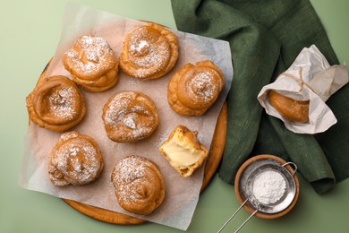 Delicious profiteroles filled with cream on green background, flat lay