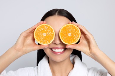 Photo of Woman in bathrobe holding juicy cut orange on light grey background. Spa treatment