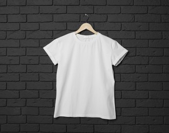 Photo of Hanger with stylish white T-shirt on black brick wall