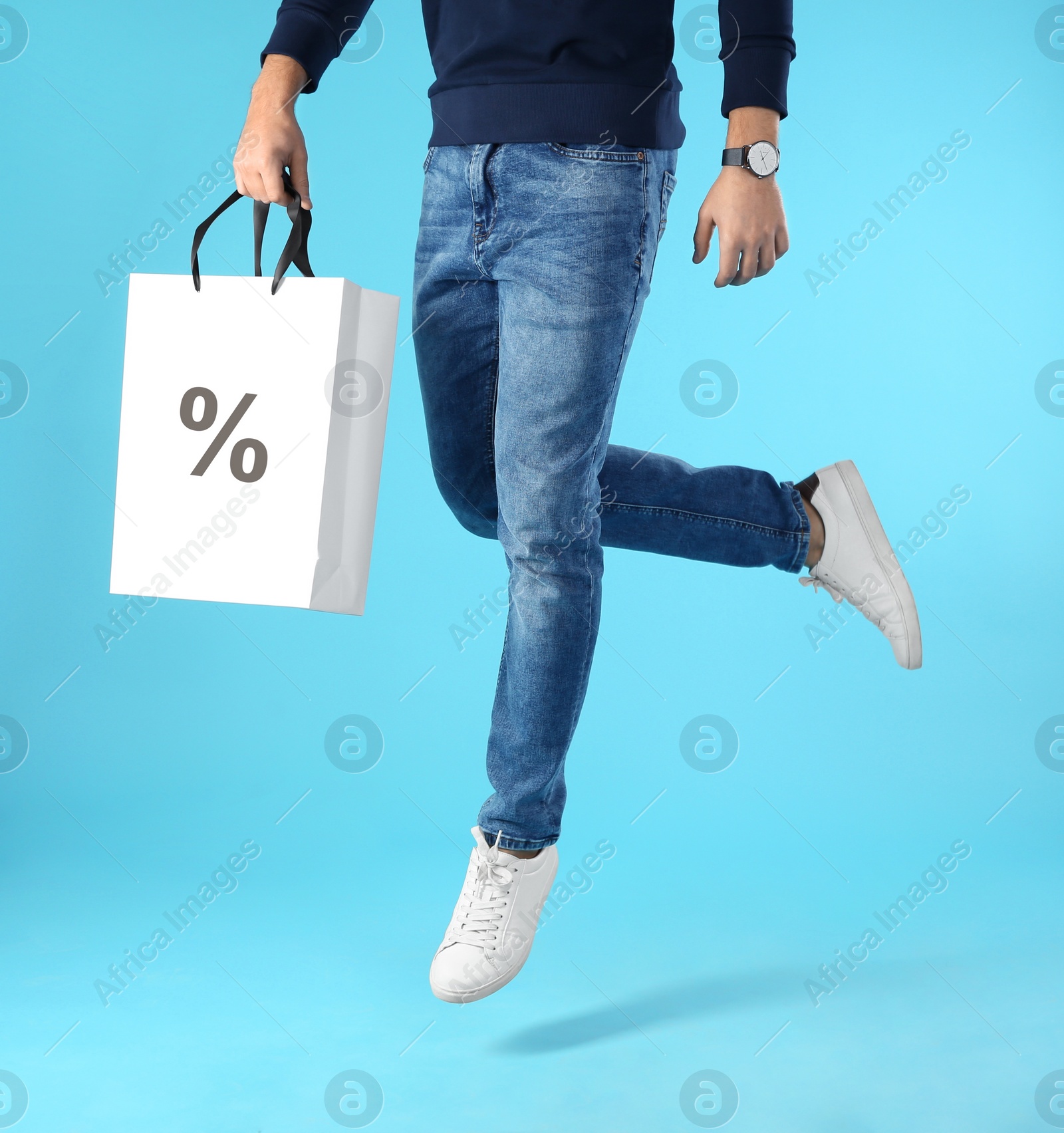 Image of Discount, sale, offer. Man jumping with shopping bag against light blue background, closeup. Paper bag with percent sign