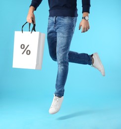 Discount, sale, offer. Man jumping with shopping bag against light blue background, closeup. Paper bag with percent sign