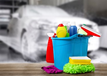 Bucket with cleaning supplies on wooden surface at car wash. Space for text