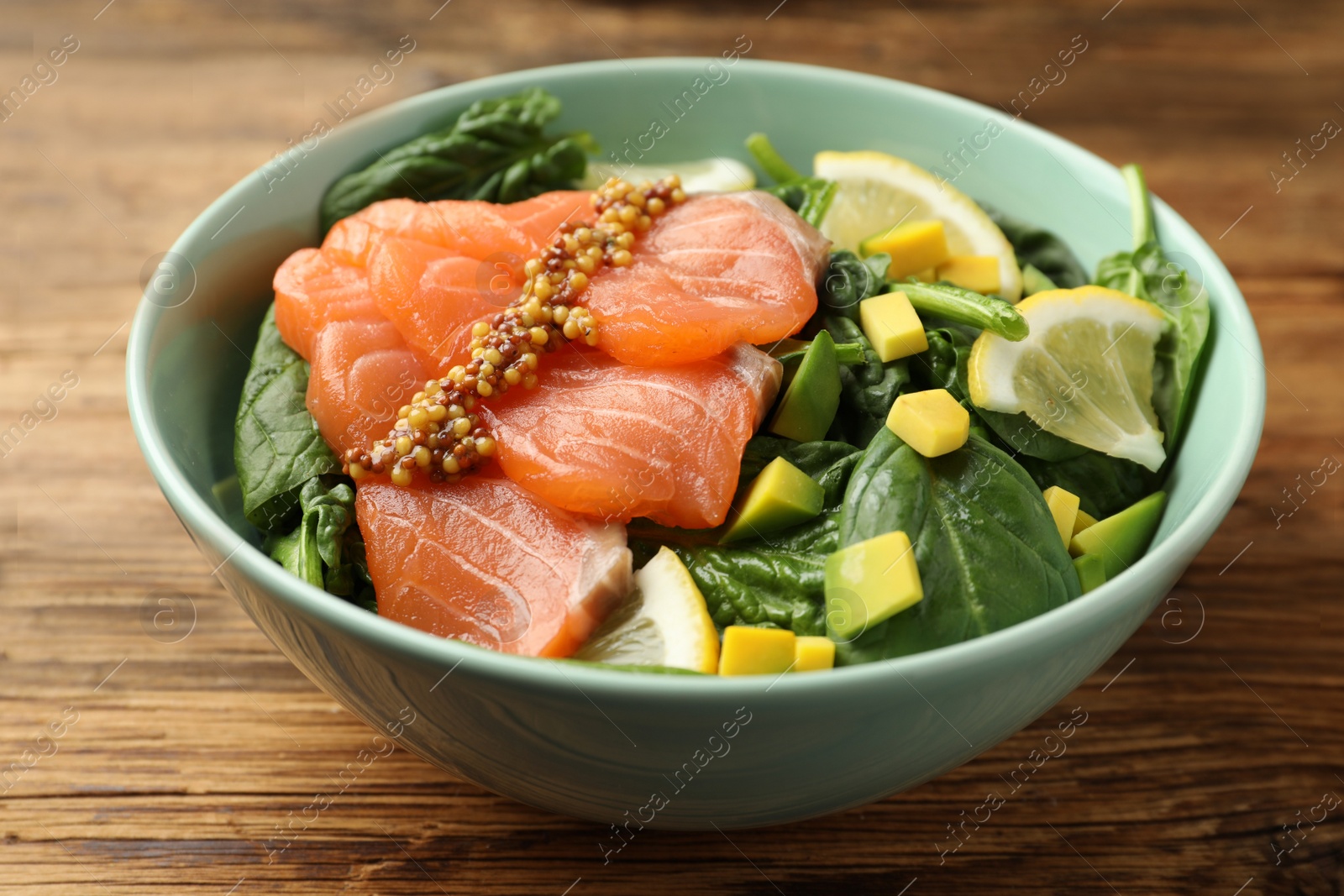 Photo of Delicious salmon with spinach, avocado and lemon in bowl on wooden table