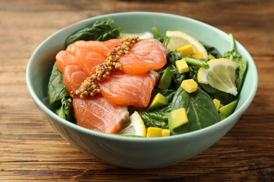 Photo of Delicious salmon with spinach, avocado and lemon in bowl on wooden table