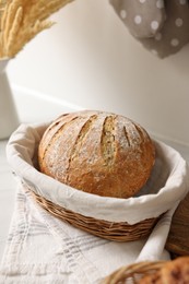 Photo of Wicker bread basket with freshly baked loaf on white marble table in kitchen