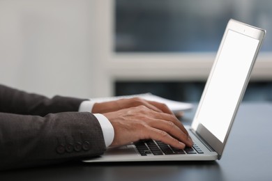 Photo of Man using modern laptop at black desk in office, closeup