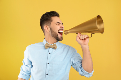Young man with megaphone on yellow background