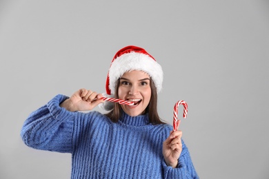 Photo of Pretty woman in Santa hat and blue sweater eating candy cane on grey background