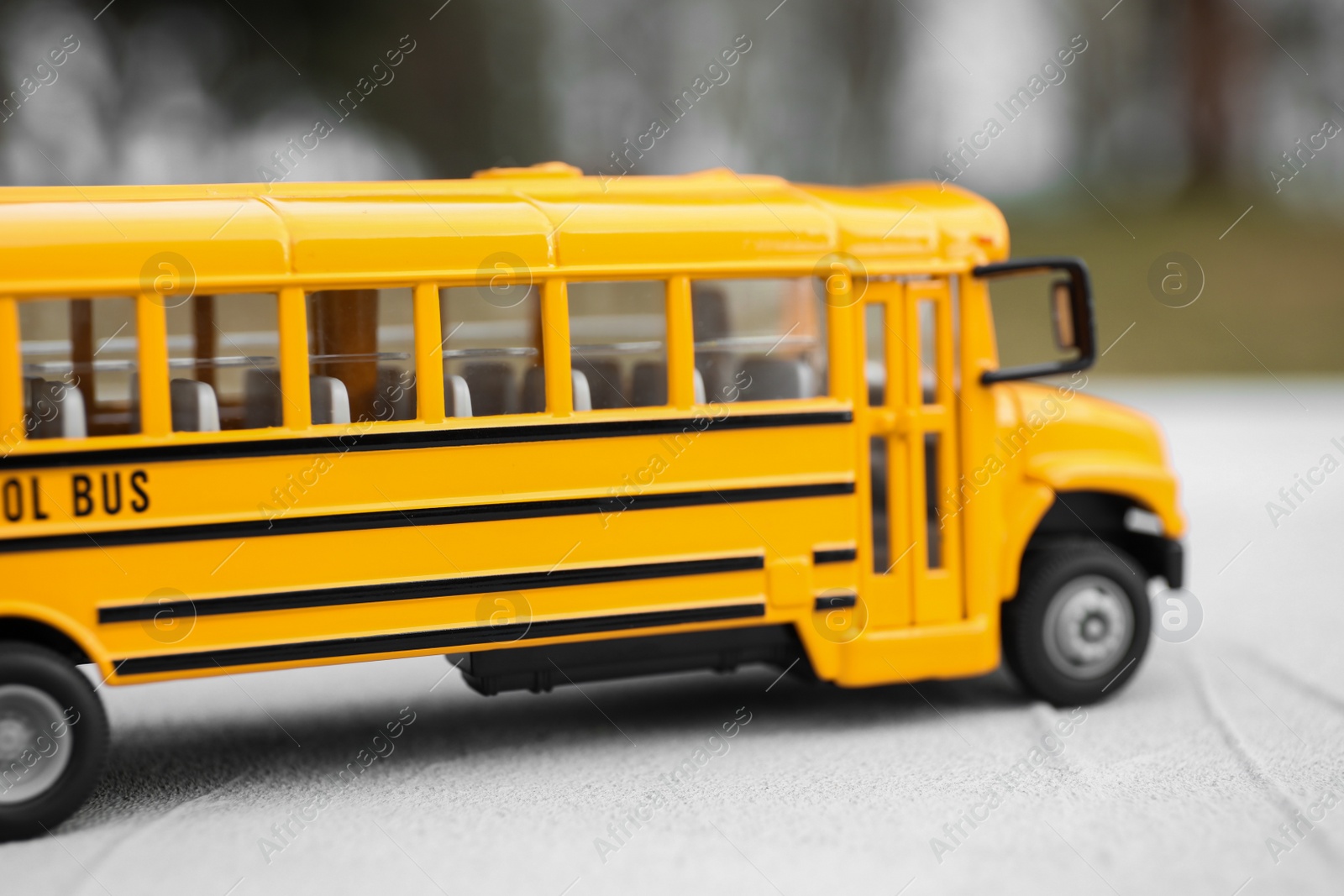 Photo of Yellow toy school bus against blurred background, closeup. Transport for students