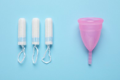 Photo of Menstrual cup and tampons on light blue background, flat lay