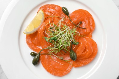 Salmon carpaccio with capers, microgreens and lemon on plate, top view