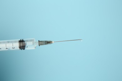 Photo of Medical syringe on light blue background, closeup. Space for text