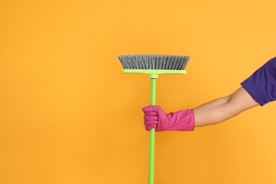 Man with green broom on orange background, closeup. Space for text