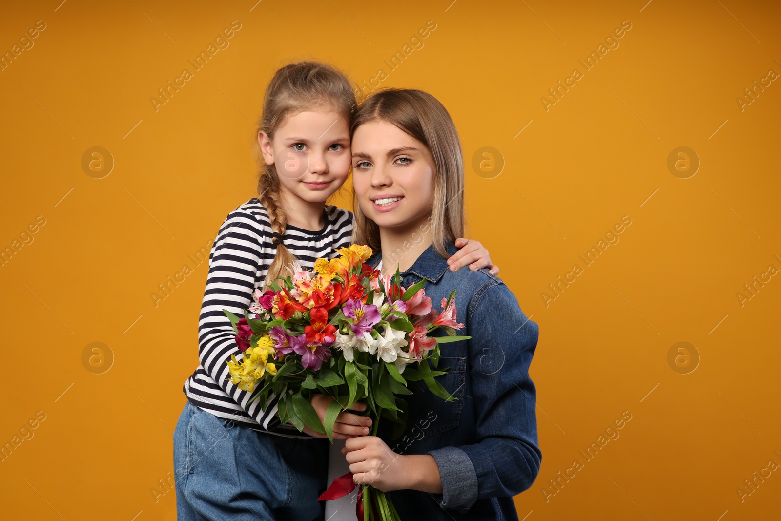 Photo of Little daughter congratulating her mom with flowers on orange background. Happy Mother's Day