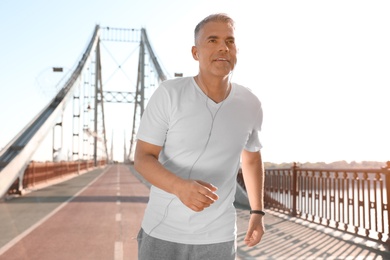Handsome mature man running on bridge, space for text. Healthy lifestyle