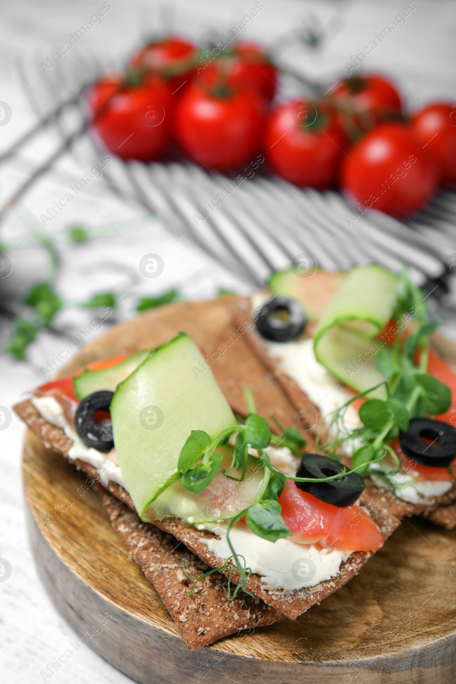 Photo of Tasty rye crispbreads with salmon, cream cheese and vegetables on white wooden table, closeup