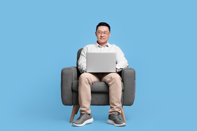 Photo of Happy man with laptop sitting in armchair on light blue background