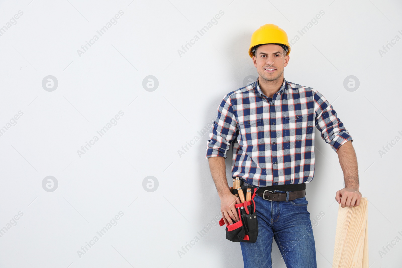 Photo of Handsome carpenter with wooden planks on light background. Space for text