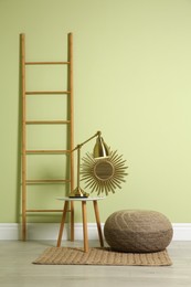 Stylish room interior with comfortable knitted pouf and decor elements near light green wall