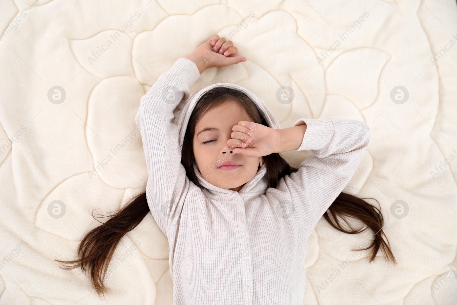 Photo of Sleepy girl in pajamas on bed, top view