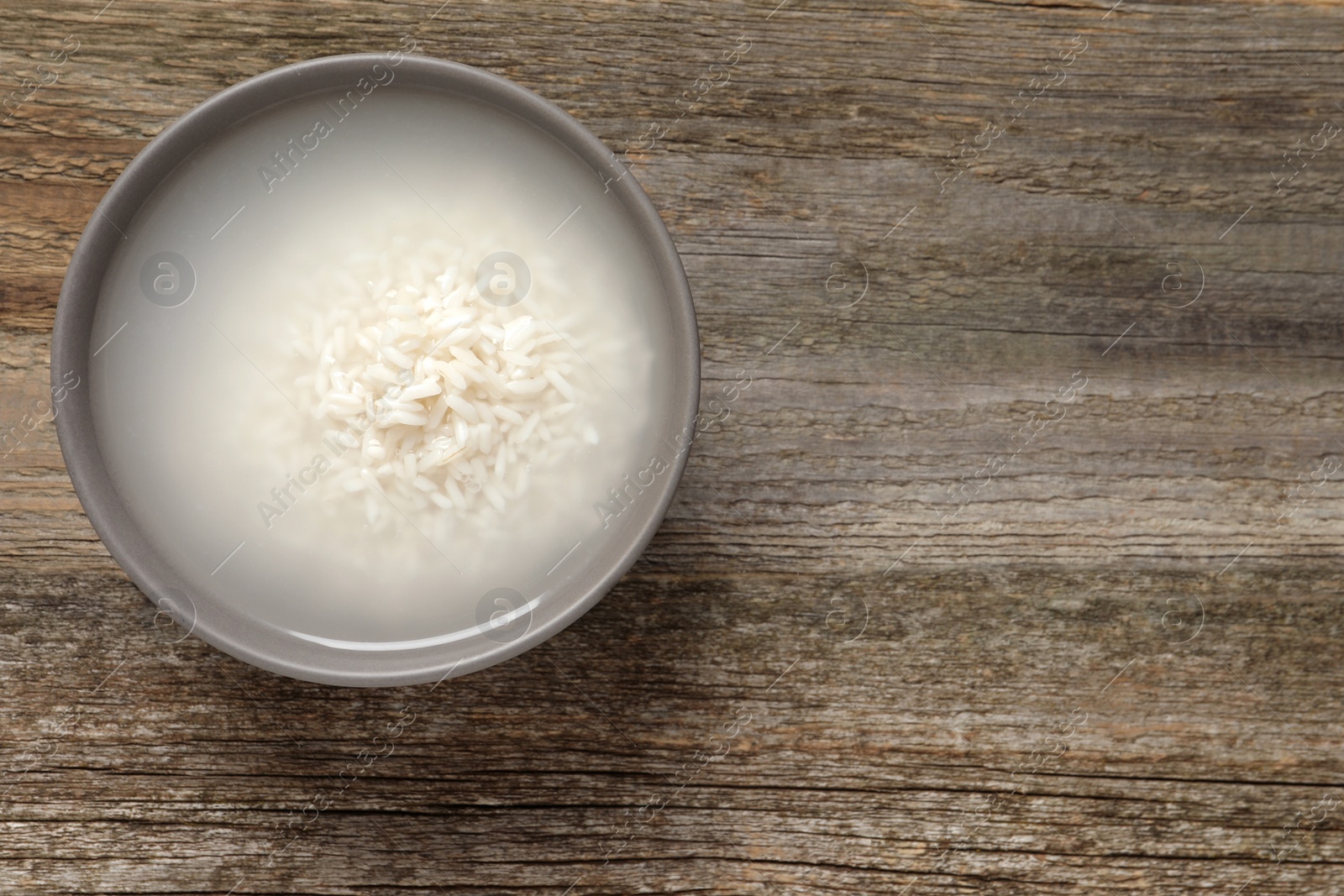 Photo of Bowl with rice soaked in water on wooden table, top view. Space for text