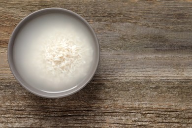 Photo of Bowl with rice soaked in water on wooden table, top view. Space for text