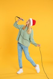 Photo of Happy woman in Santa Claus hat singing with microphone on yellow background. Christmas music