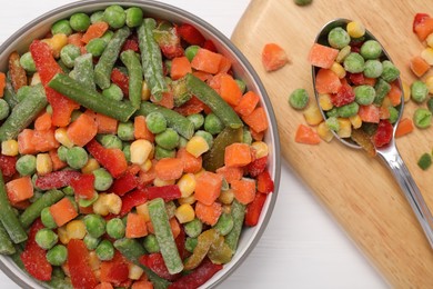 Mix of different frozen vegetables in bowl on white wooden table, top view