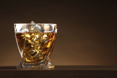 Photo of Whiskey with ice cubes in glass on table against brown background. Space for text