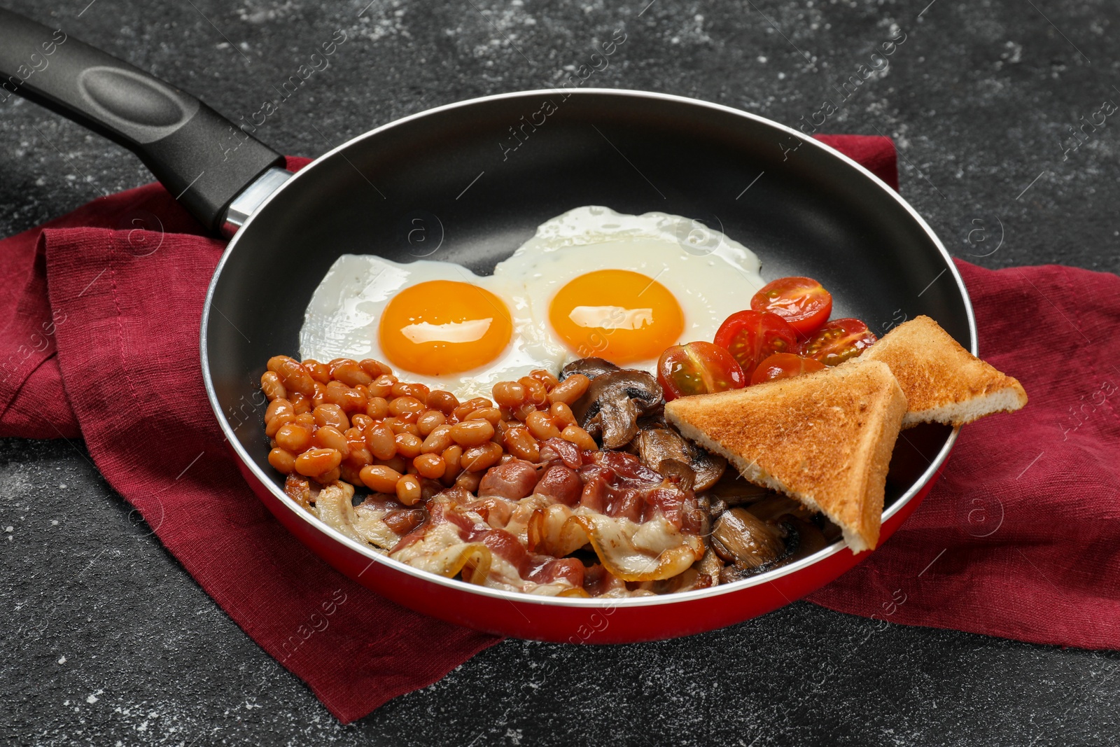 Photo of Frying pan with cooked traditional English breakfast on black textured table, closeup