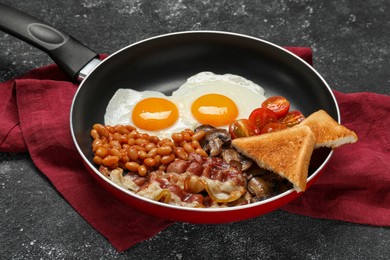 Frying pan with cooked traditional English breakfast on black textured table, closeup