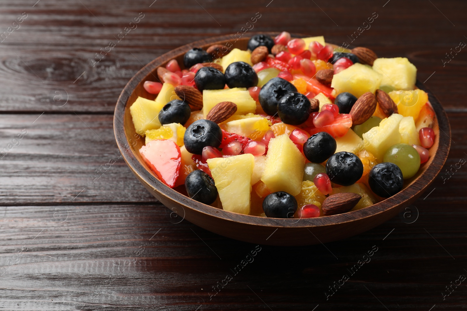 Photo of Delicious fruit salad in bowl on wooden table