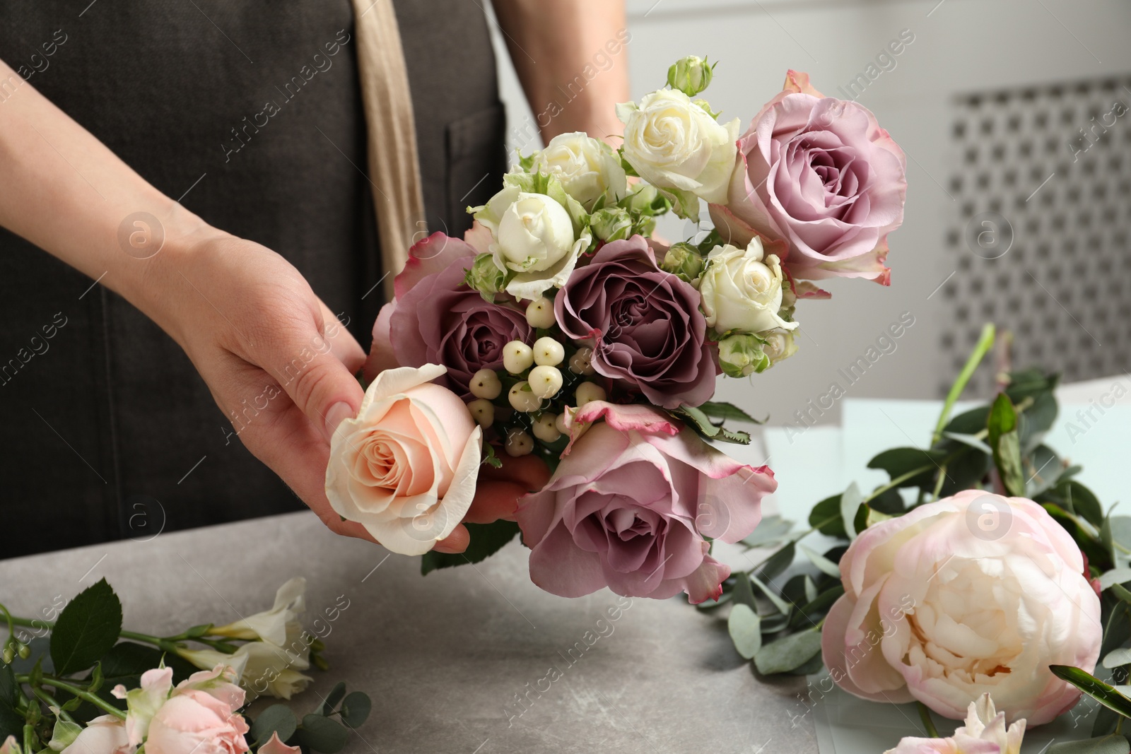 Photo of Florist creating beautiful bouquet at light grey table indoors, closeup