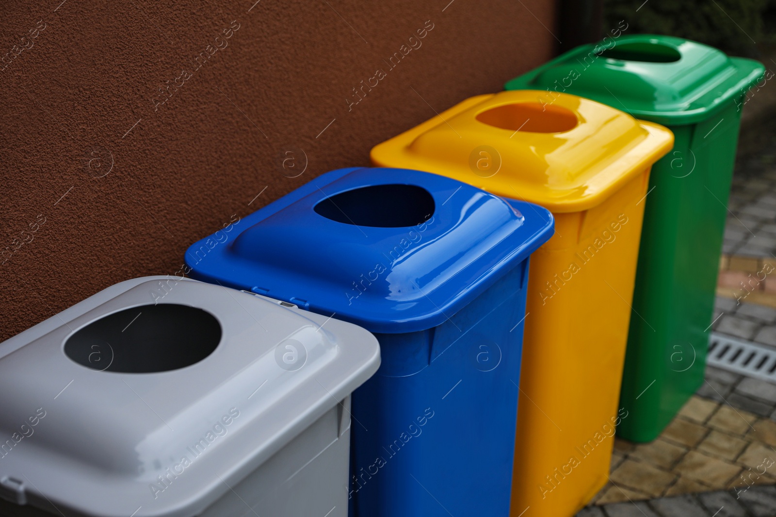 Photo of Many color recycling bins near brown wall outdoors